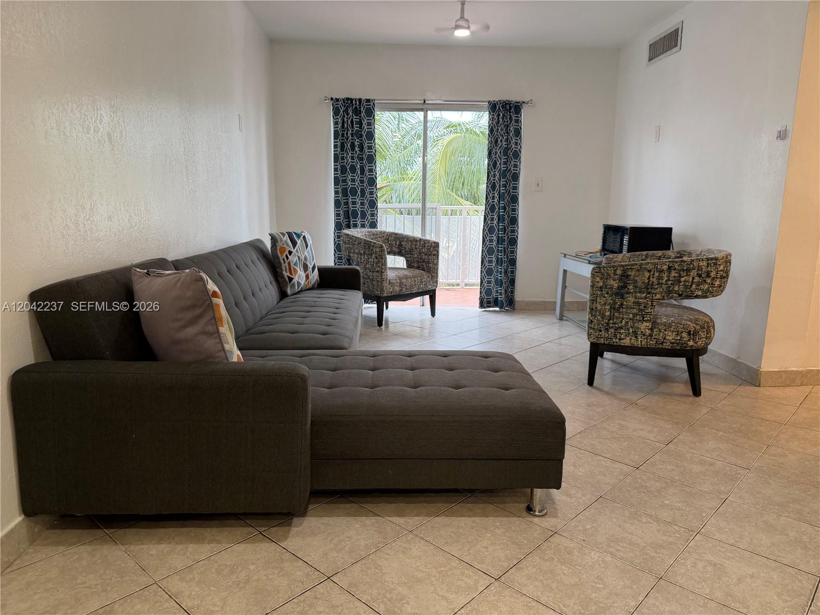 A living room features a gray sectional sofa, two patterned armchairs, and tile flooring — NORTH MIAMI BEACH, FL
