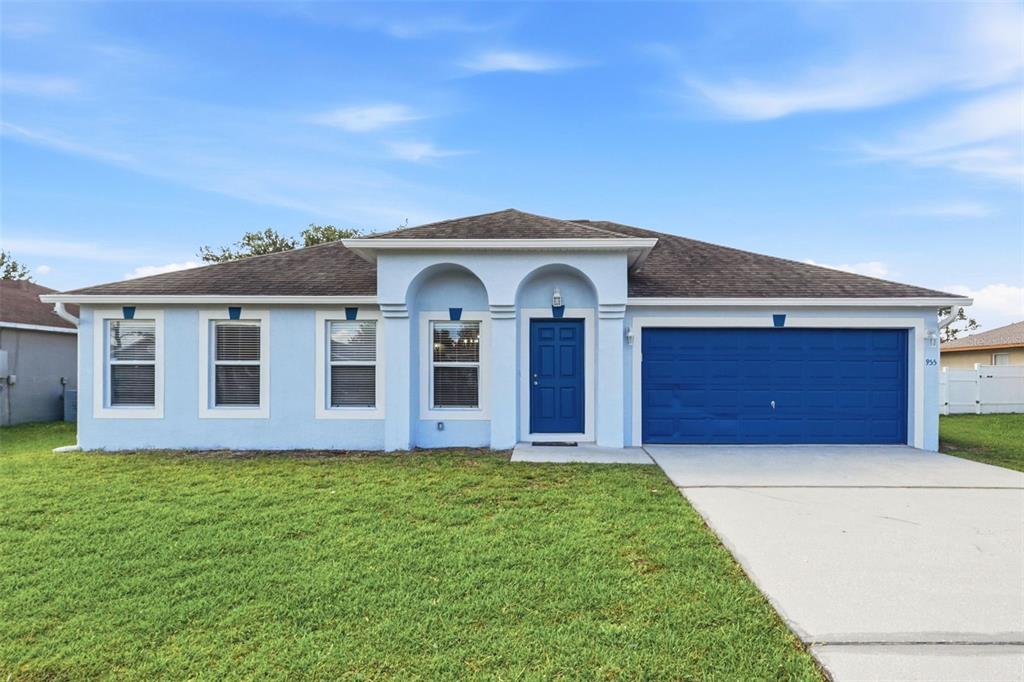 A single-story house with light blue stucco, a blue front door, and a two-car garage — 955 LOUVRE COURT, KISSIMMEE, FL