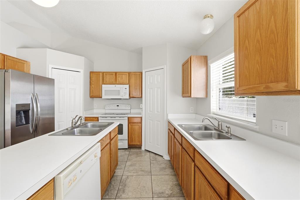A kitchen features wood cabinets, white countertops, stainless steel appliances, and tile flooring — 955 LOUVRE COURT, KISSIMMEE, FL