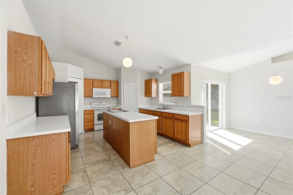 A kitchen with wood cabinets, white countertops, a center island, and tile flooring — 955 LOUVRE COURT, KISSIMMEE, FL