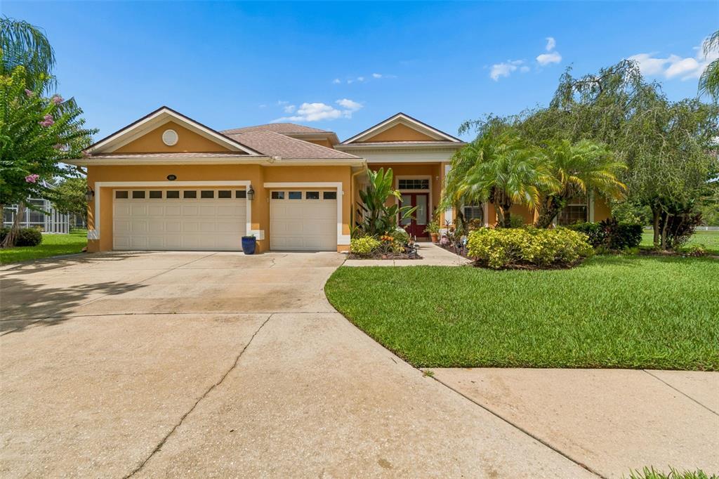 A single-story house with a tan exterior, a three-car garage, and a landscaped front yard — 5303 CLOUDS PEAK DRIVE, LUTZ, FL