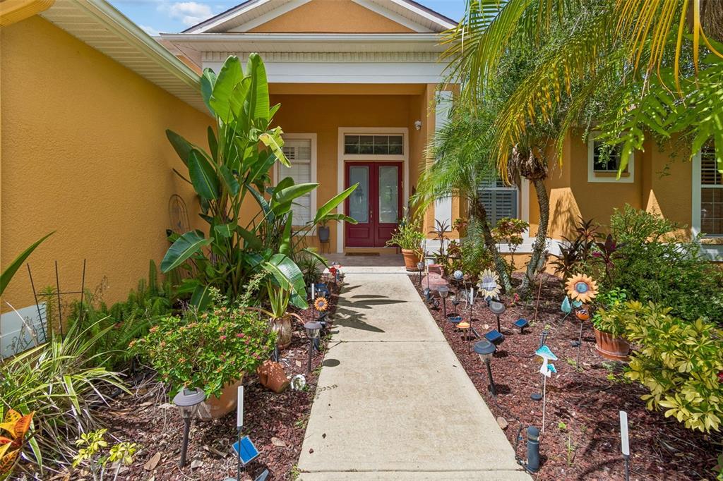 A concrete walkway leads to the red double front doors of a yellow stucco house — 5303 CLOUDS PEAK DRIVE, LUTZ, FL