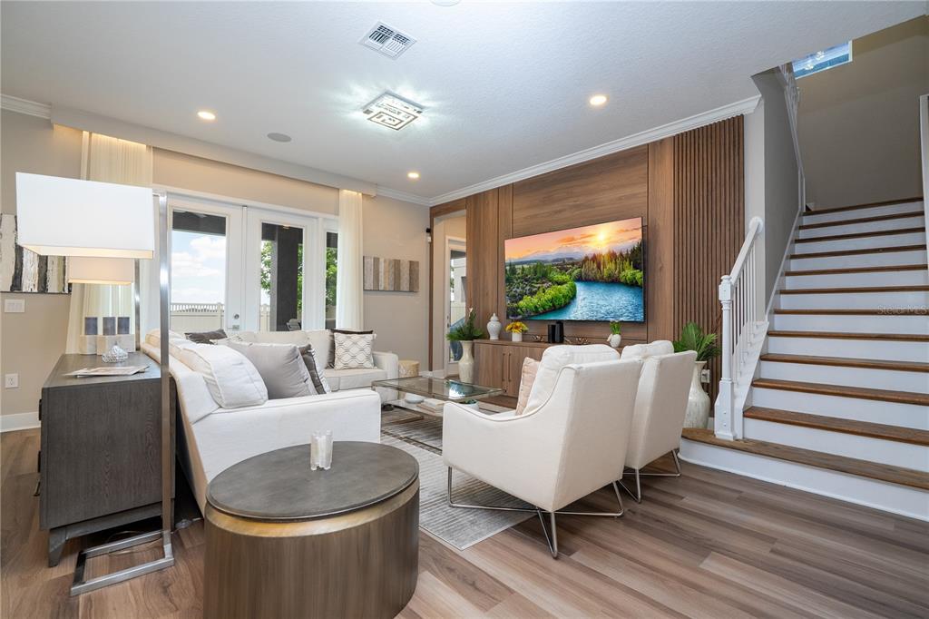A living room features a wood-paneled accent wall, a television, white seating, and a staircase — 9942 SUMMERLAKE GROVES STREET, WINTER GARDEN, FL