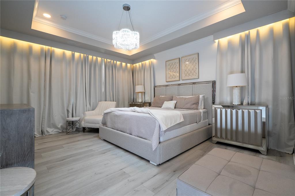 A modern bedroom features a gray upholstered bed, mirrored nightstands, and floor-to-ceiling curtains with lighting — 9942 SUMMERLAKE GROVES STREET, WINTER GARDEN, FL
