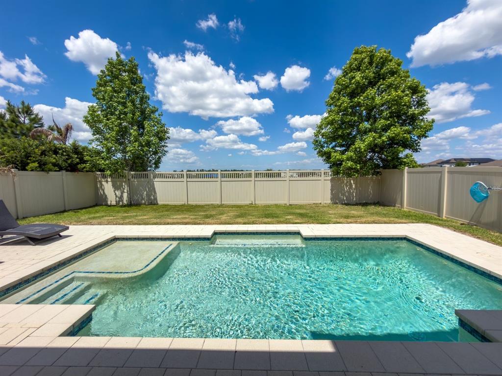 A backyard features a rectangular swimming pool with a tanning ledge and a vinyl fence — 9942 SUMMERLAKE GROVES STREET, WINTER GARDEN, FL