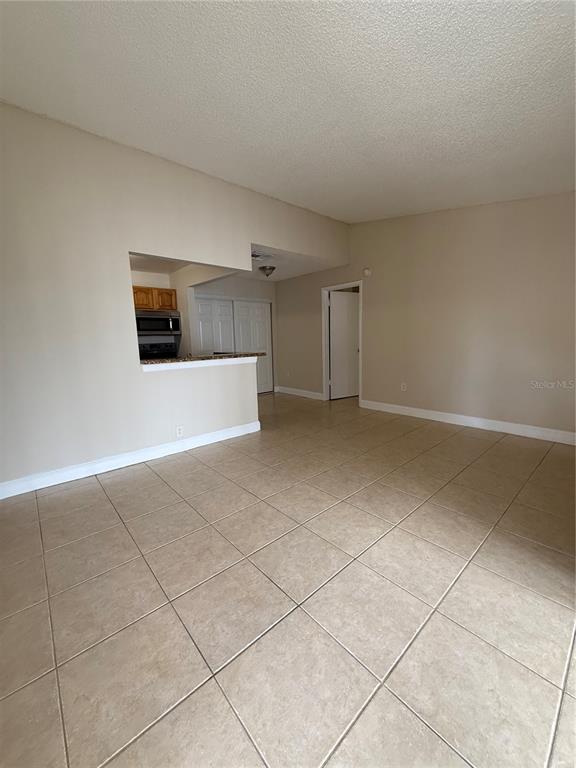 An open-concept living area features beige tile flooring, neutral walls, and a kitchen pass-through window — 3831 BOWLINE CIRCLE UNIT 204, KISSIMMEE, FL