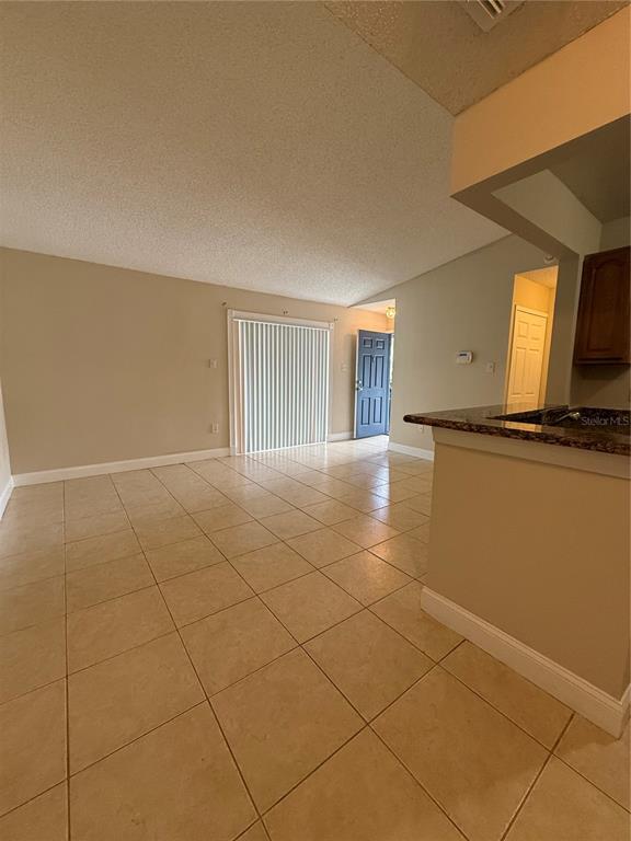 An open-concept living area features light-colored tile flooring, beige walls, and a sliding glass door — 3831 BOWLINE CIRCLE UNIT 204, KISSIMMEE, FL