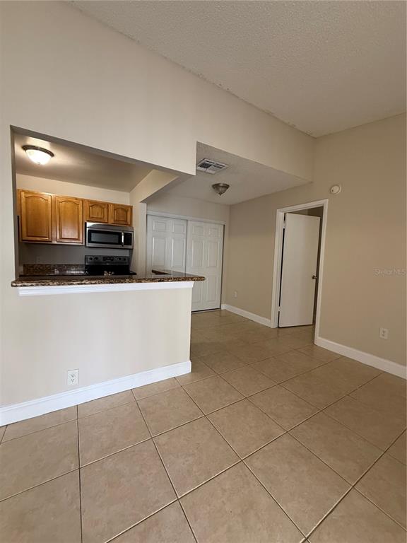 A kitchen with wooden cabinets and a breakfast bar overlooks a tiled living area — 3831 BOWLINE CIRCLE UNIT 204, KISSIMMEE, FL