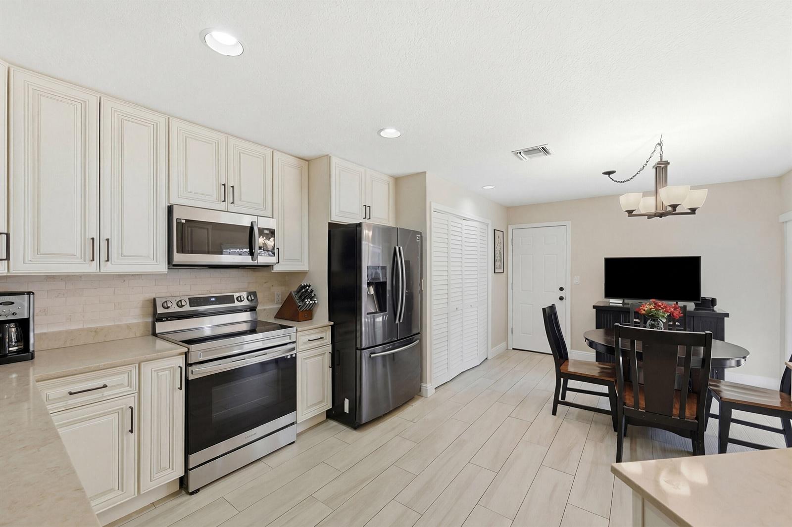 A kitchen with cream cabinets, stainless steel appliances, and a dining area with a television — 4115 Carriage Drive # P2, Pompano Beach FL 33069, POMPANO BEACH, FL