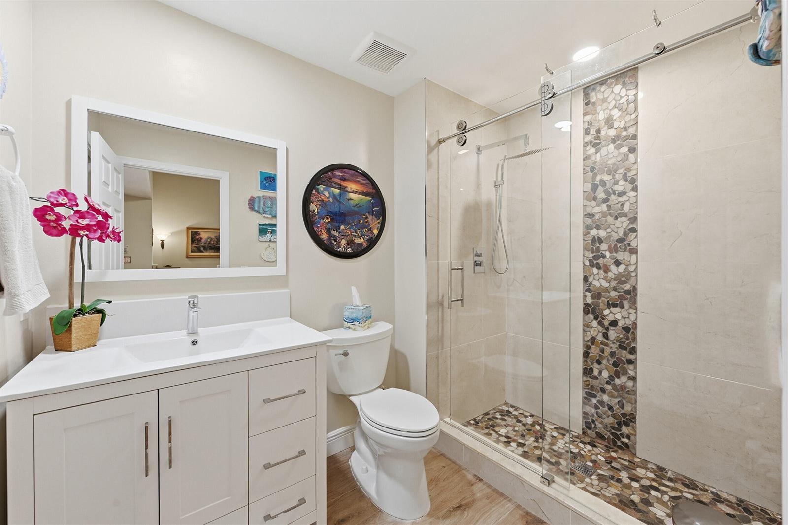 A bathroom features a white vanity, a toilet, and a glass-enclosed shower with pebble accents — 4115 Carriage Drive # P2, Pompano Beach FL 33069, POMPANO BEACH, FL