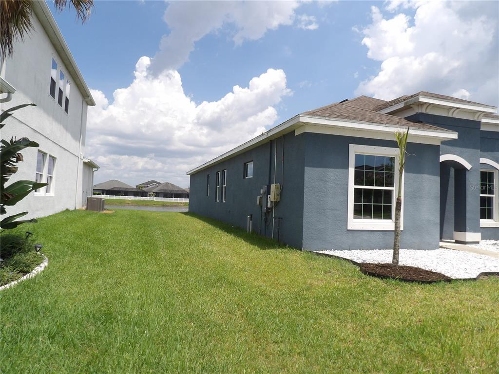 A side view of a blue house exterior with a grassy yard and a pond — 11940 SUNBURST MARBLE ROAD, RIVERVIEW, FL
