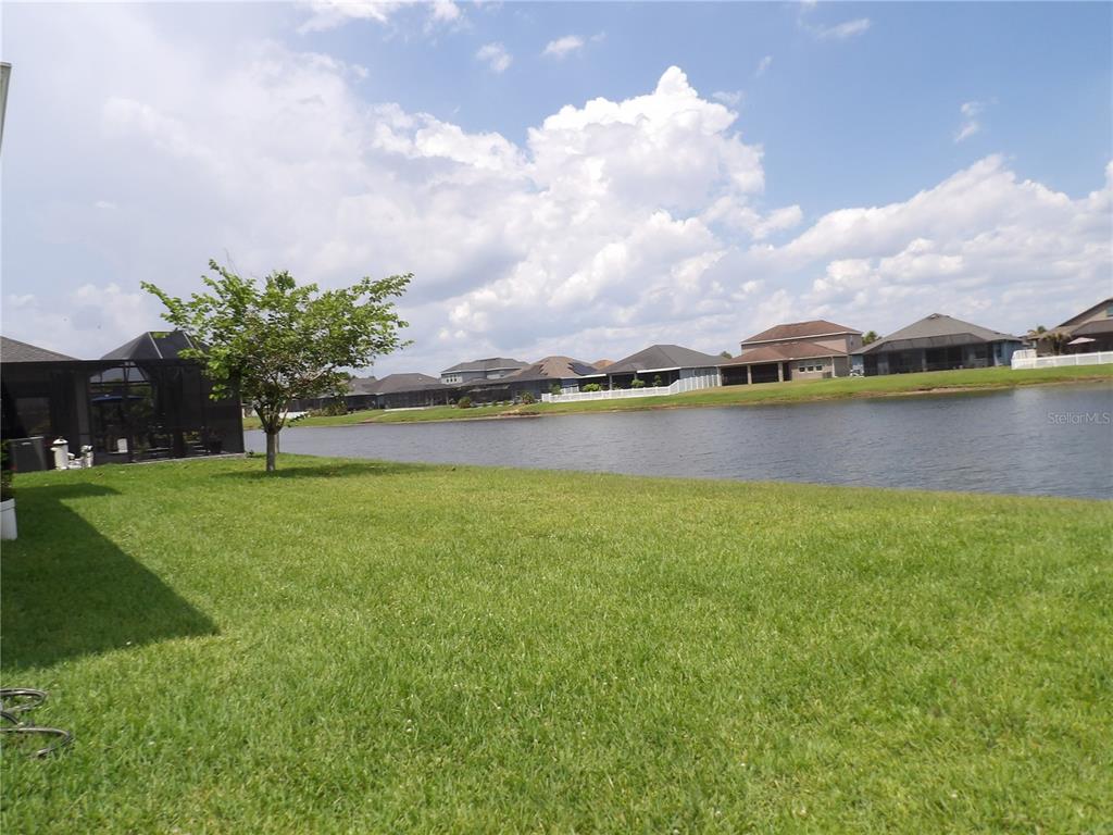 A grassy backyard overlooks a lake with several houses visible on the opposite shore — 11940 SUNBURST MARBLE ROAD, RIVERVIEW, FL