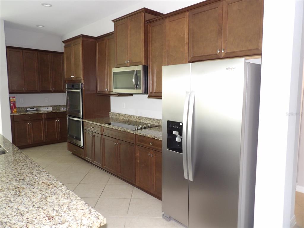A kitchen features dark wood cabinets, granite countertops, stainless steel appliances, and tile flooring — 11940 SUNBURST MARBLE ROAD, RIVERVIEW, FL