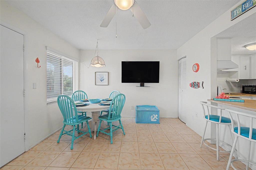 A dining area with a round table, turquoise chairs, a wall-mounted television, and tile flooring — 2110 GULF BOULEVARD UNIT 9, INDIAN ROCKS BEACH, FL
