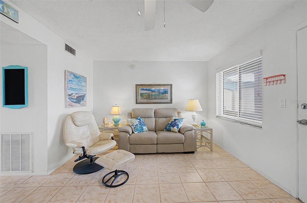 A living room features a beige sofa, a matching recliner with ottoman, and tile flooring — 2110 GULF BOULEVARD UNIT 9, INDIAN ROCKS BEACH, FL