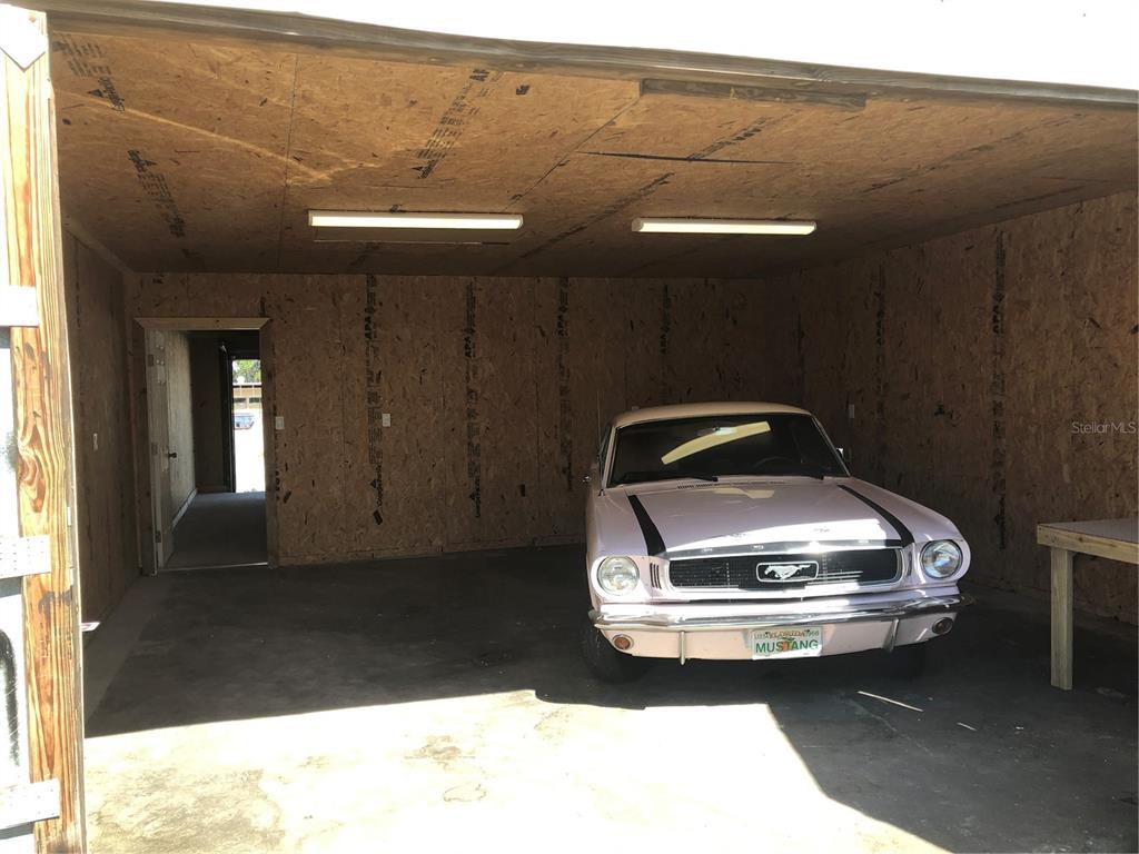 A light pink vintage Ford Mustang is parked inside a garage with unfinished plywood walls — 712 N RIDGEWOOD DRIVE, SEBRING, FL