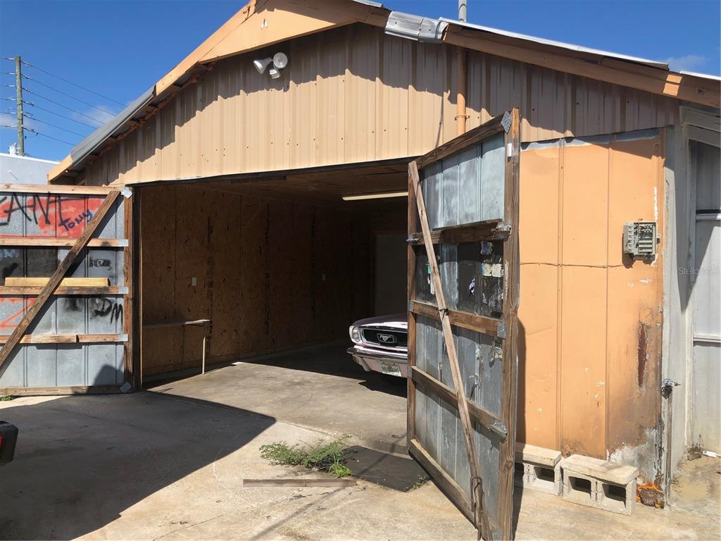 An open garage with metal doors and wood-paneled walls houses a vintage car — 712 N RIDGEWOOD DRIVE, SEBRING, FL