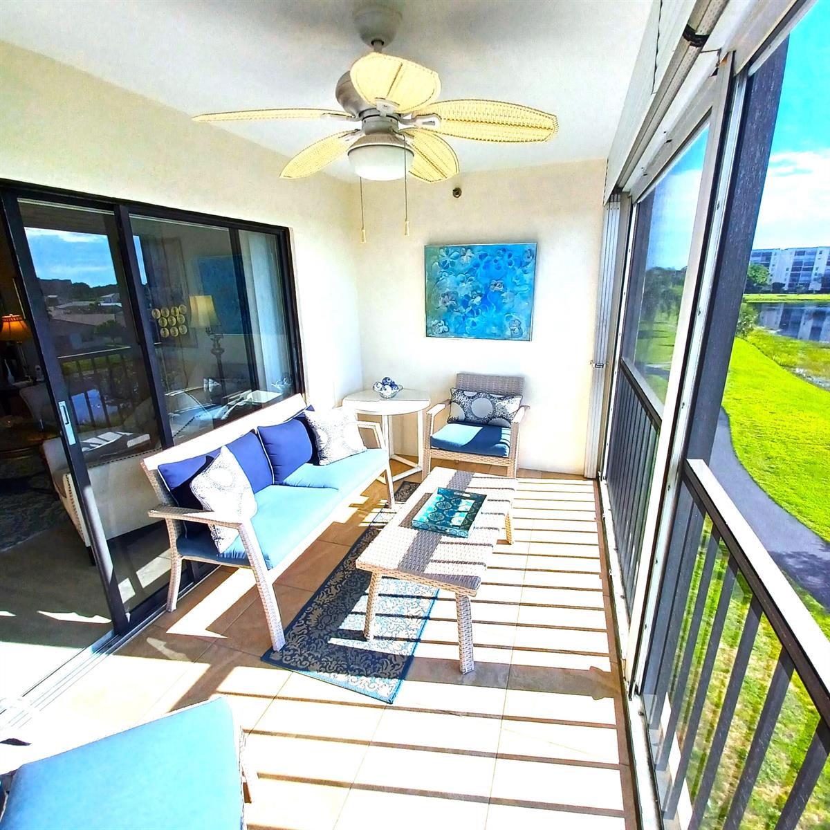A screened-in balcony features wicker furniture, a ceiling fan, and a view of a pond — 7260 Kinghurst Drive # 406, Delray Beach FL 33446, DELRAY BEACH, FL