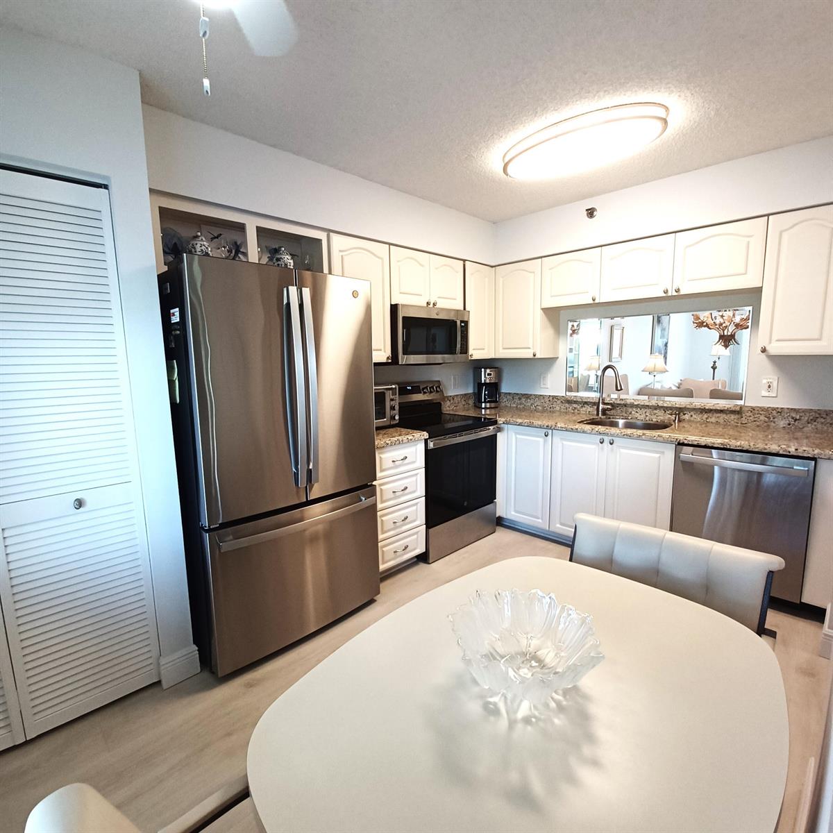 A kitchen features white cabinets, stainless steel appliances, granite countertops, and a dining table — 7260 Kinghurst Drive # 406, Delray Beach FL 33446, DELRAY BEACH, FL