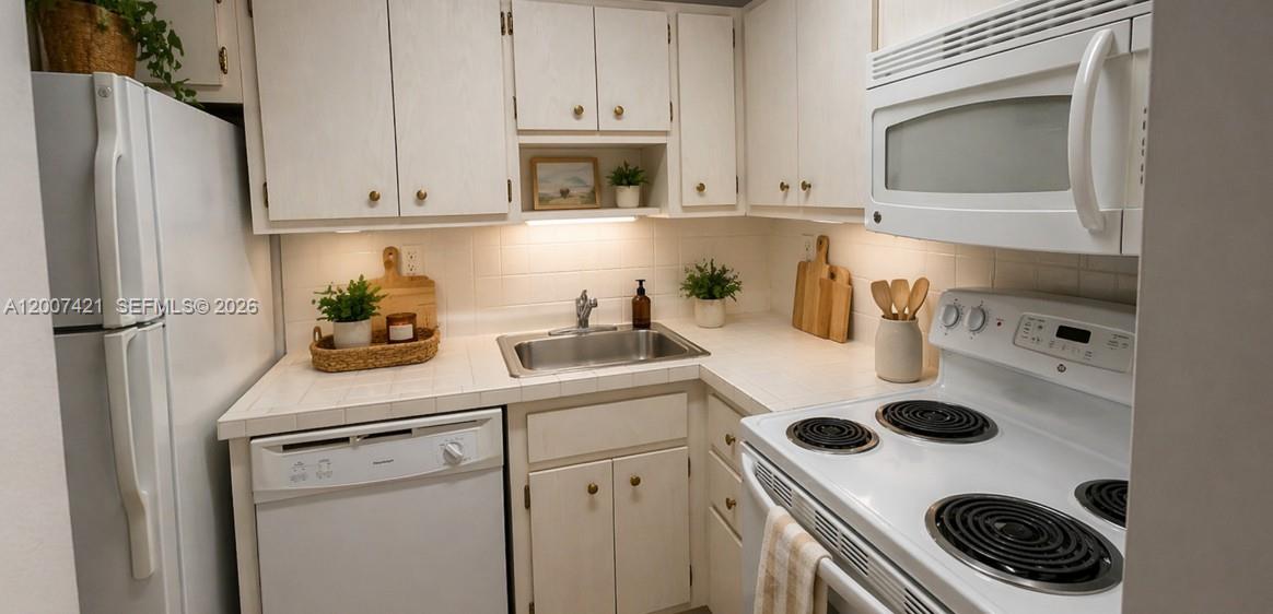 A small kitchen features white cabinets, white appliances, and tiled countertops — 2899 Collins Ave # 1040, Miami Beach FL 33140, MIAMI BEACH, FL