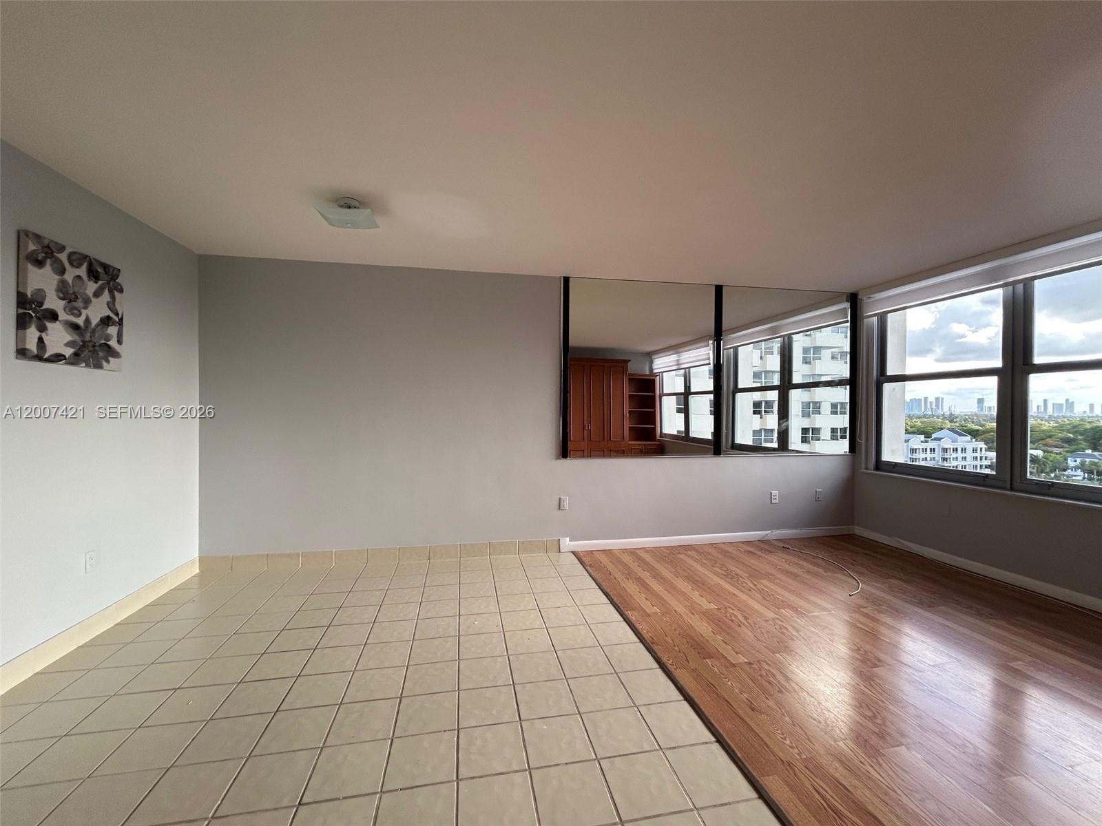 An empty room features a tiled floor, a wood-floored area, wall mirrors, and large windows — 2899 Collins Ave # 1040, Miami Beach FL 33140, MIAMI BEACH, FL