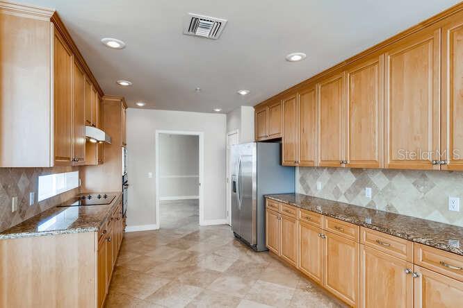 A kitchen features light wood cabinets, granite countertops, a stainless steel refrigerator, and tiled flooring — 8749 THE ESPLANADE UNIT 32, ORLANDO, FL