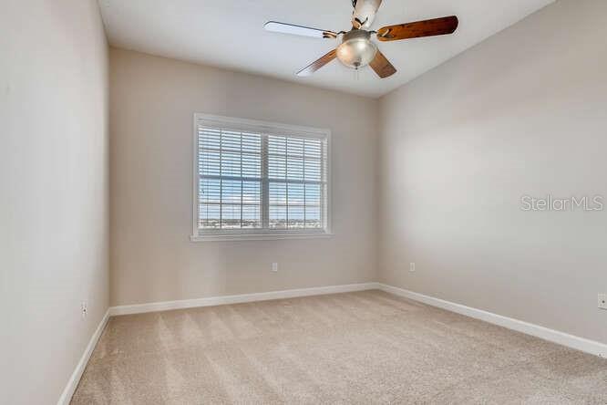 An empty bedroom features beige walls, neutral carpeting, a ceiling fan, and a large window — 8749 THE ESPLANADE UNIT 32, ORLANDO, FL