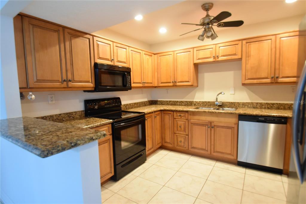 A kitchen with wood cabinets, granite countertops, stainless steel dishwasher, and black appliances — 1601 PELICAN POINT DRIVE UNIT HA215, SARASOTA, FL