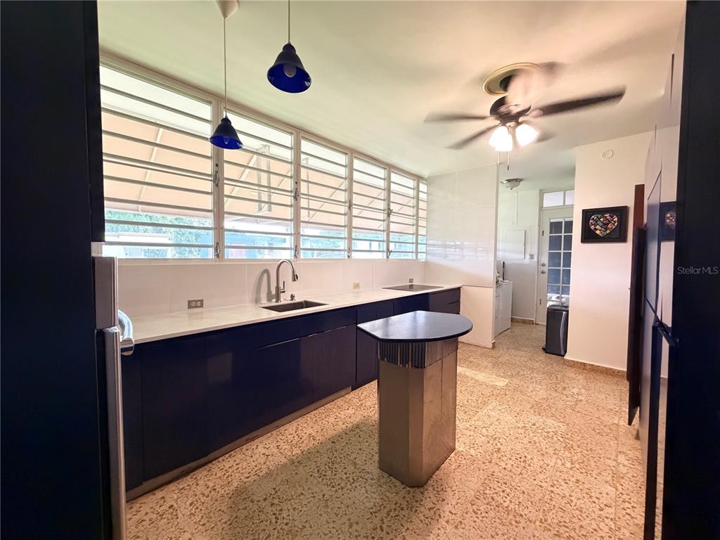 A kitchen features dark blue cabinets, a white countertop, a small island, and louvered windows — Lot 119 VILLA SONSIRE, MAYAGUEZ, PR