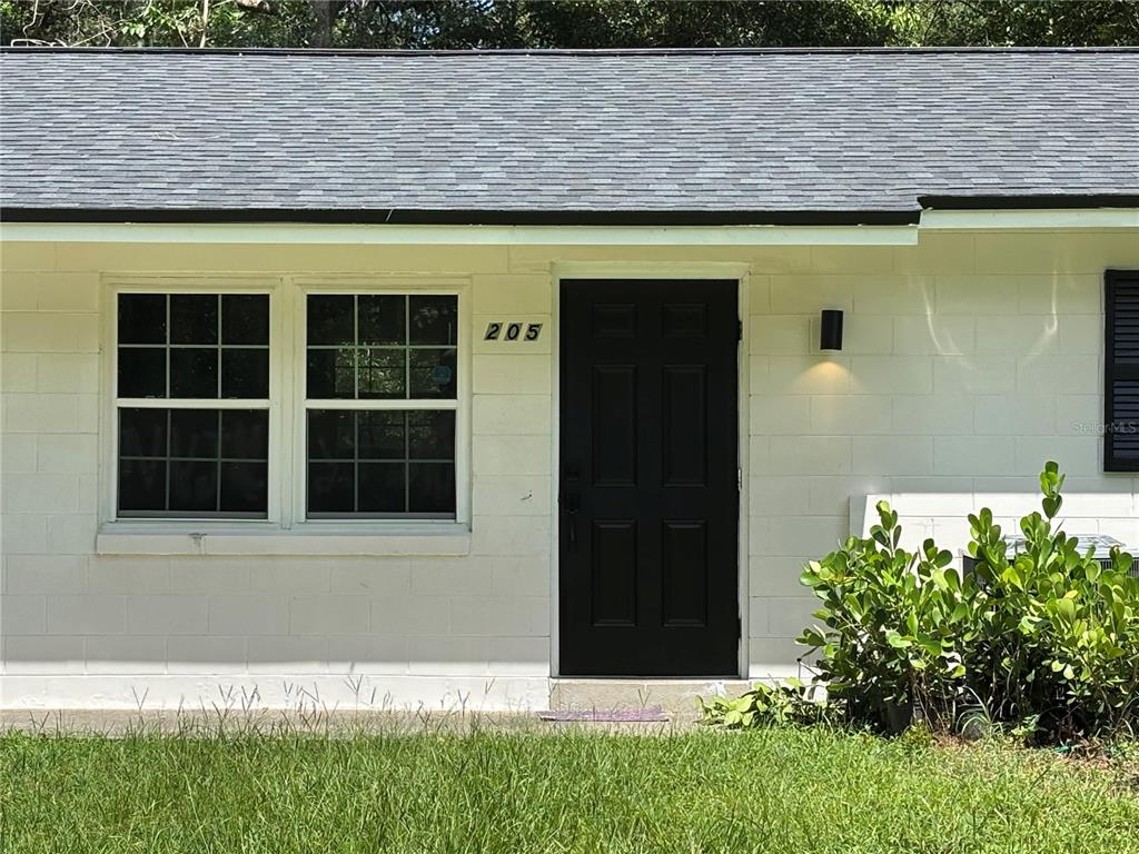 A white concrete block house exterior features a black front door and a double window — 205 S CHANDLER AVENUE, DELAND, FL