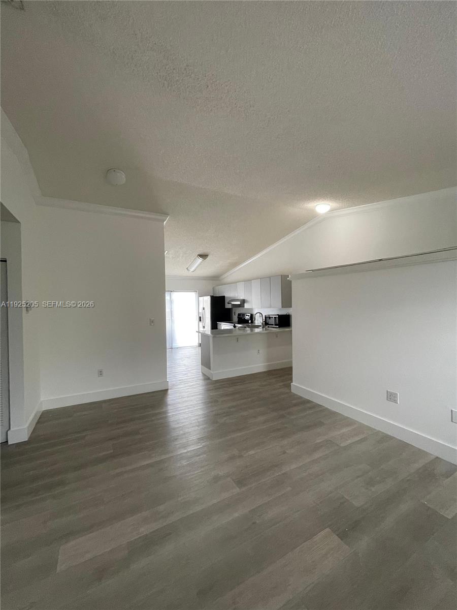 A living area with light wood-look flooring leads to an open kitchen with white cabinets — 3375 W 76th St # 211, Hialeah FL 33018, HIALEAH, FL