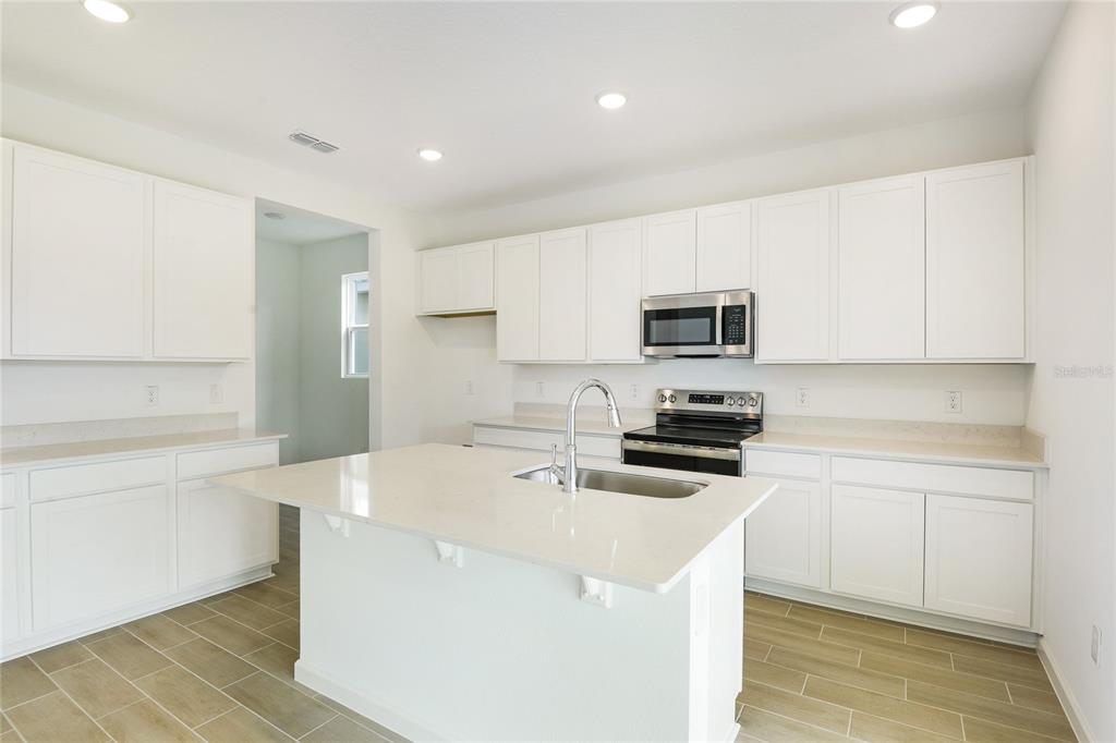 A modern kitchen features white cabinets, quartz countertops, a central island, and stainless steel appliances — 334 ALEXANDRITE STREET, DELAND, FL