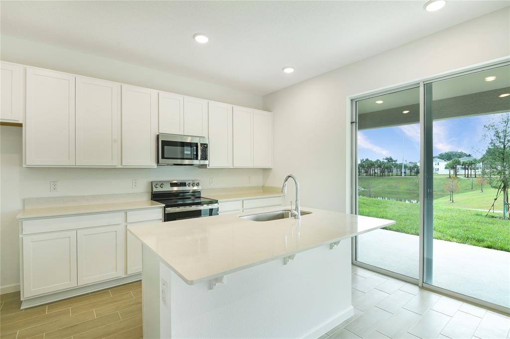 A modern kitchen features white cabinets, quartz countertops, a center island, and sliding glass doors — 334 ALEXANDRITE STREET, DELAND, FL