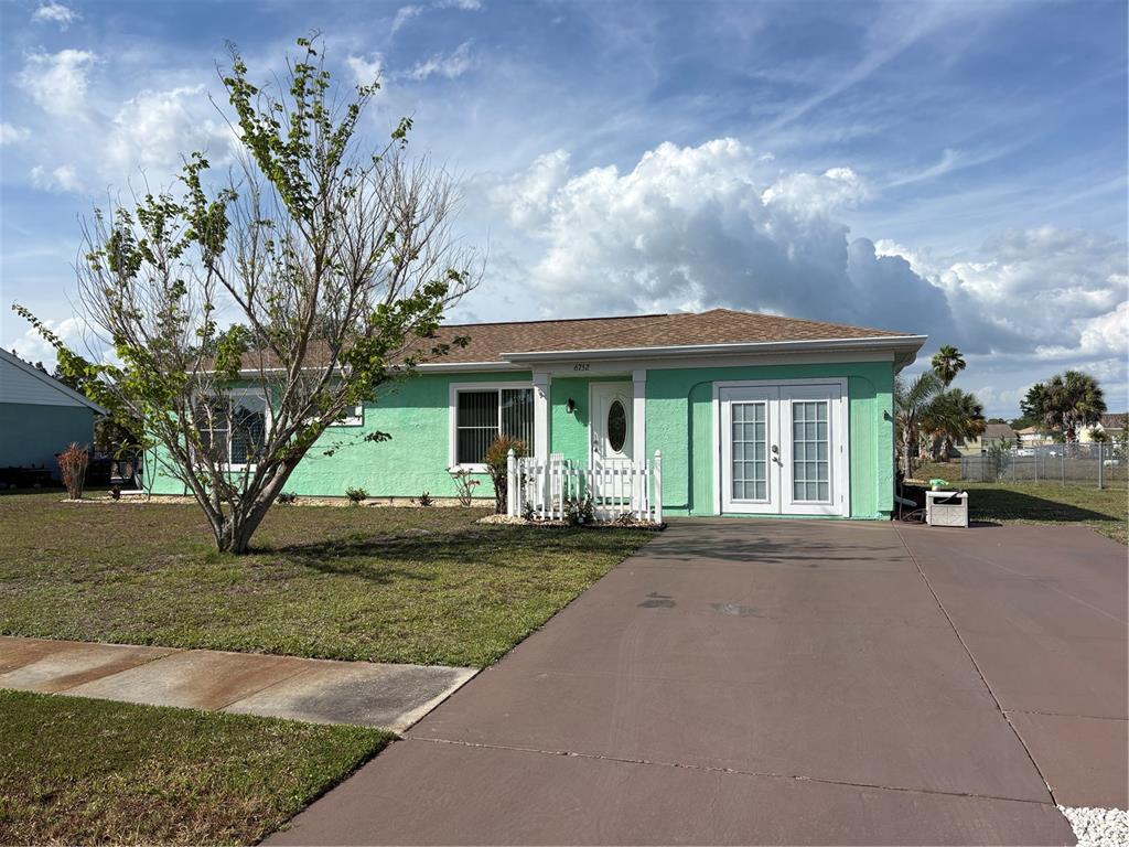 A single-story house with mint green stucco walls, a brown roof, and a concrete driveway — 6752 DENNISON AVENUE, NORTH PORT, FL