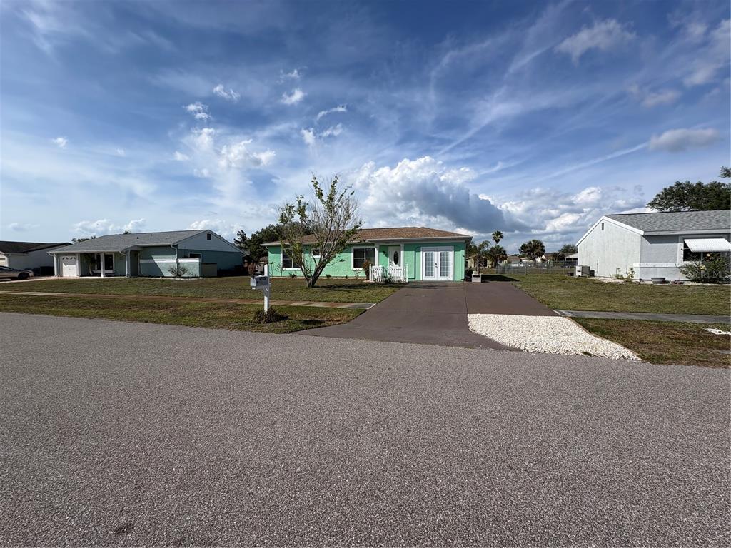 A light green single-story house with a driveway and a front yard under a blue sky — 6752 DENNISON AVENUE, NORTH PORT, FL