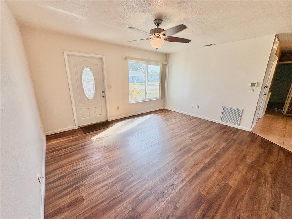 An empty living room features wood-look flooring, a ceiling fan, a front door, and a window — 6752 DENNISON AVENUE, NORTH PORT, FL