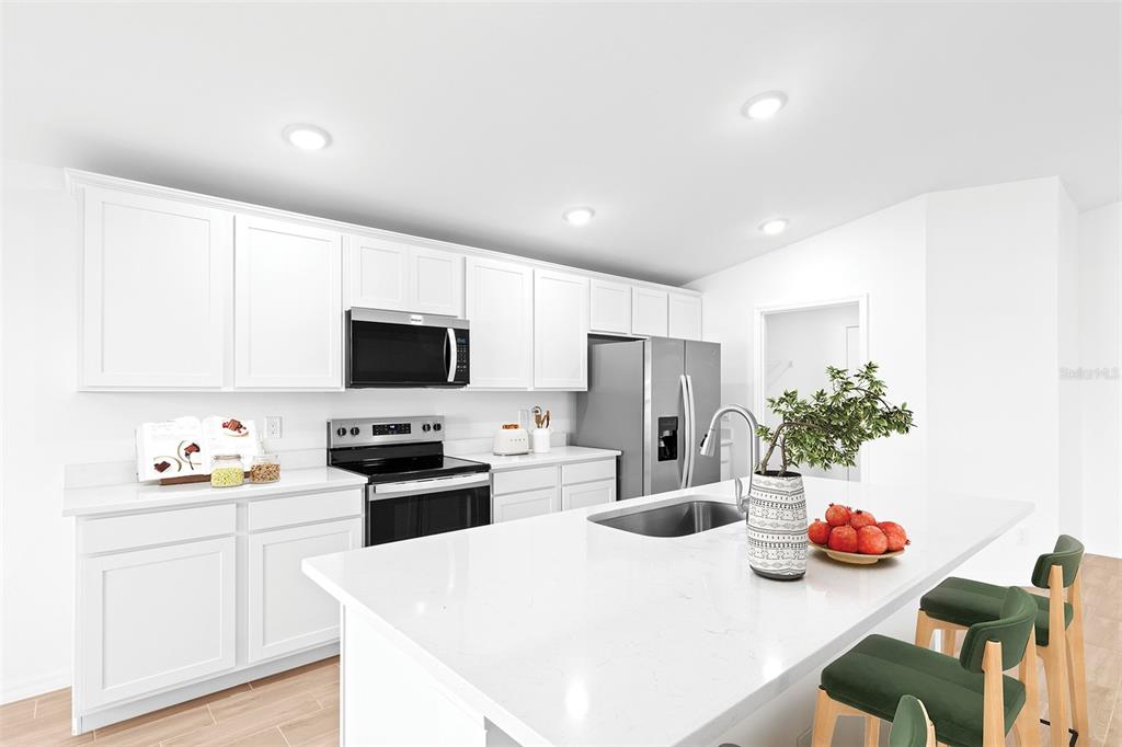 A modern kitchen features white cabinetry, stainless steel appliances, and a large quartz-topped island — 15122 CANNELL LANE, PORT CHARLOTTE, FL