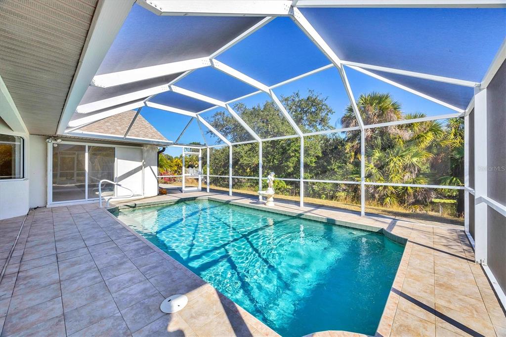 A screened-in swimming pool patio features tiled flooring and a view of palm trees — 1236 NATRONA DRIVE, NORTH PORT, FL