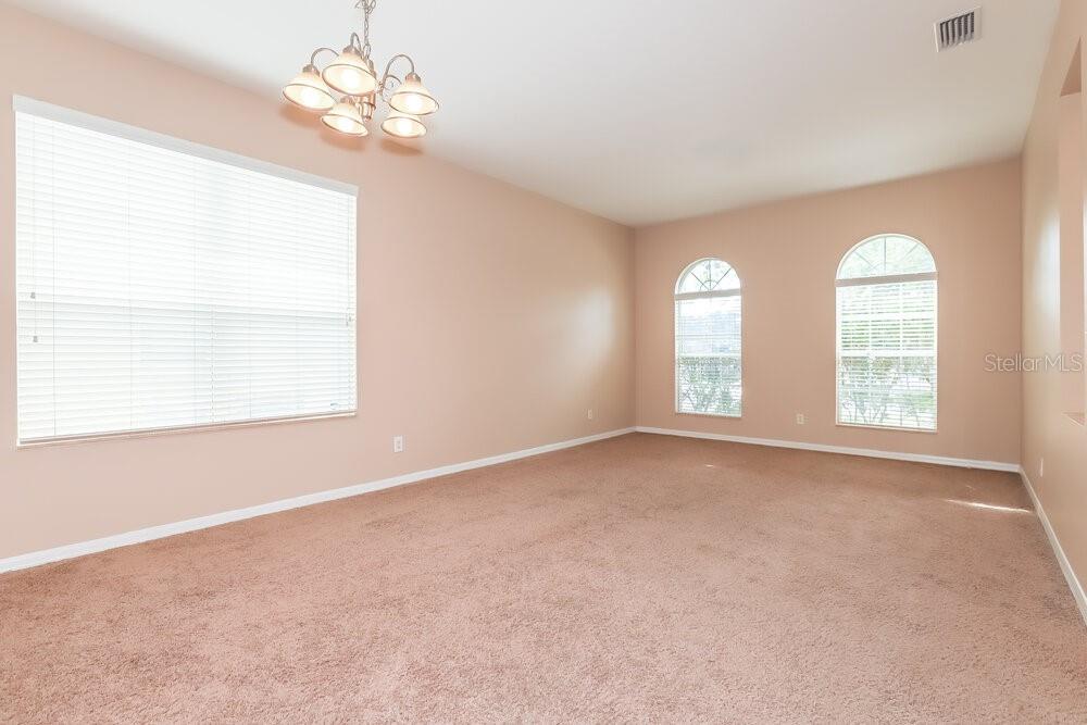 An empty room with beige walls, tan carpet, a chandelier, and three windows — 513 9TH STREET NE, RUSKIN, FL