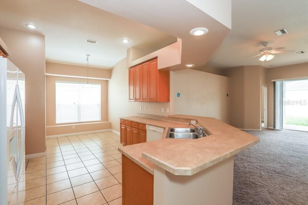 A kitchen with light-colored tile flooring, wood cabinets, and a peninsula counter overlooking a living area — 513 9TH STREET NE, RUSKIN, FL