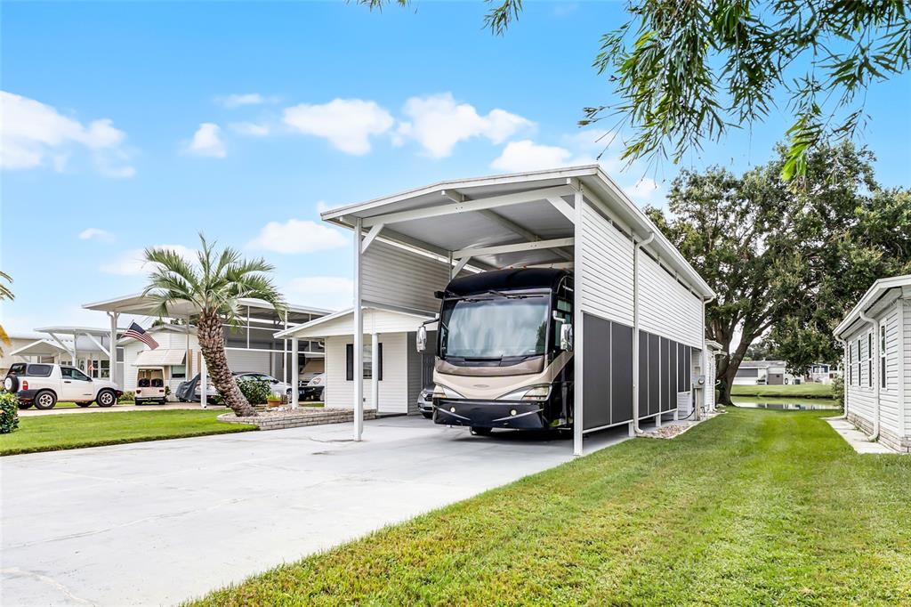 A large recreational vehicle is parked under a tall metal carport next to a house — 5001 MOUNT OLIVE SHORES DRIVE, POLK CITY, FL