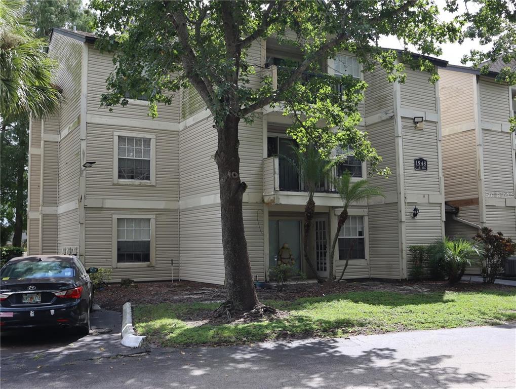 A three-story apartment building with beige siding and a large tree in the front yard — 1948 LAKE ATRIUMS CIRCLE UNIT 118, ORLANDO, FL