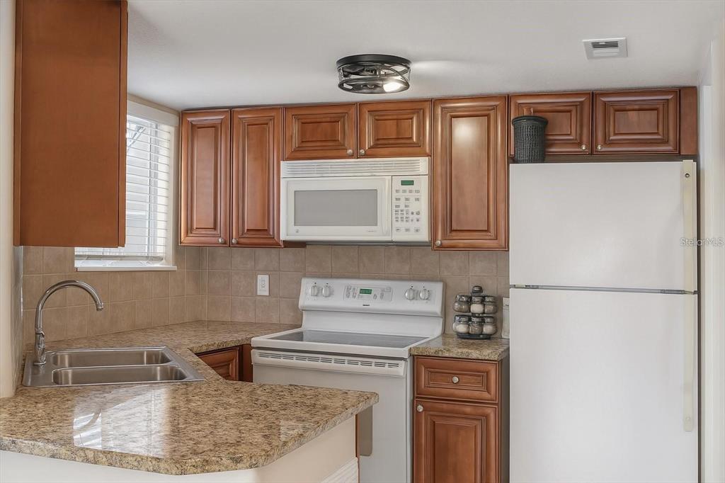 A kitchen features wood cabinets, granite countertops, white appliances, and a double-basin sink — 1948 LAKE ATRIUMS CIRCLE UNIT 118, ORLANDO, FL