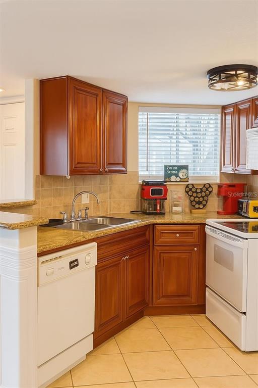 A kitchen features wood cabinets, granite countertops, white appliances, and a tiled floor — 1948 LAKE ATRIUMS CIRCLE UNIT 118, ORLANDO, FL