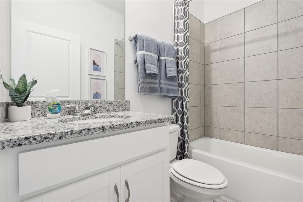 A bathroom features a granite vanity, white cabinets, a toilet, and a tiled shower-tub combo — 3812 RISING TRAIL, DAVENPORT, FL