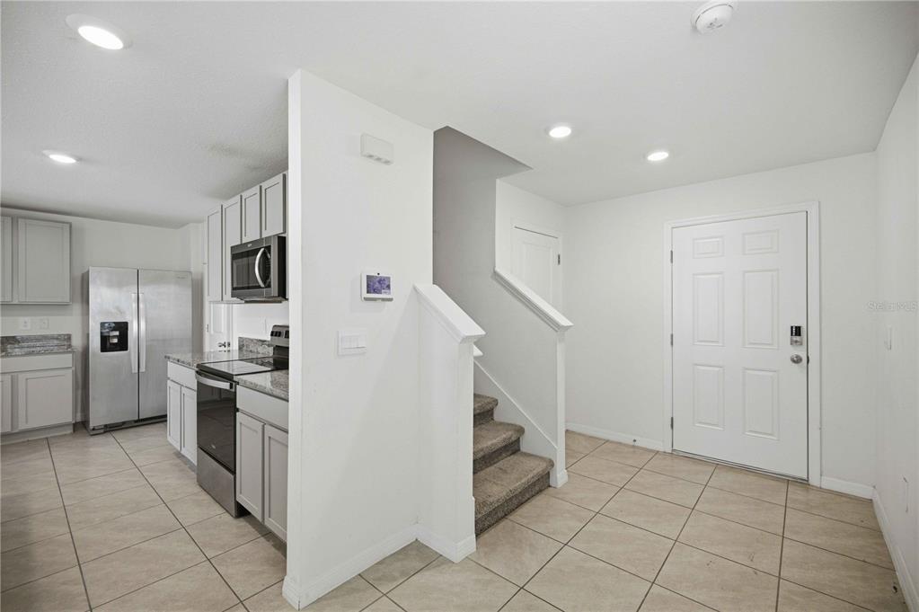A kitchen with gray cabinets and stainless steel appliances sits next to a carpeted staircase — 8642 SW 46TH AVENUE, OCALA, FL