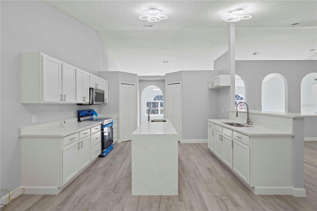 A modern kitchen features white cabinets, a central island, and light wood-look flooring — 941 JAYHIL DRIVE, MINNEOLA, FL