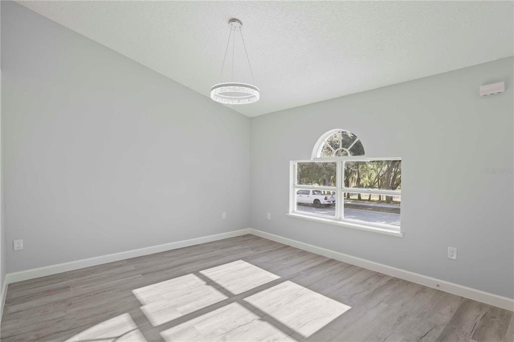 An empty room features light gray walls, wood-look flooring, a modern chandelier, and an arched window — 941 JAYHIL DRIVE, MINNEOLA, FL
