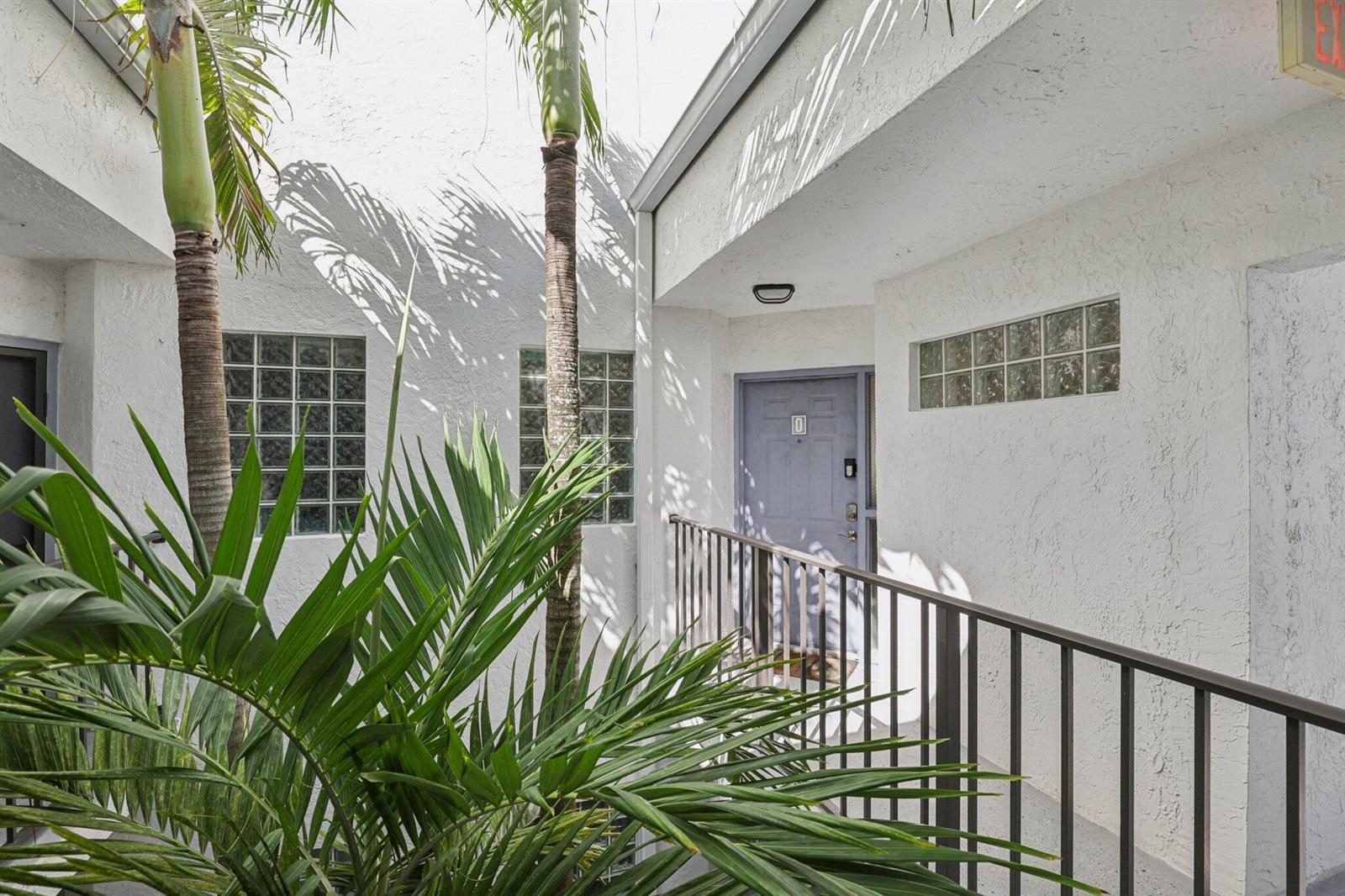 An exterior view of a building entrance with a blue door, palm trees, and railing — 5394 Firenze Drive # O, Boynton Beach FL 33437, BOYNTON BEACH, FL
