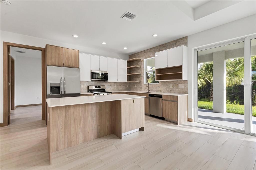 A modern kitchen features light wood cabinets, white upper cabinets, quartz countertops, and a sliding door — 405 SUNSET ROAD N, ROTONDA WEST, FL